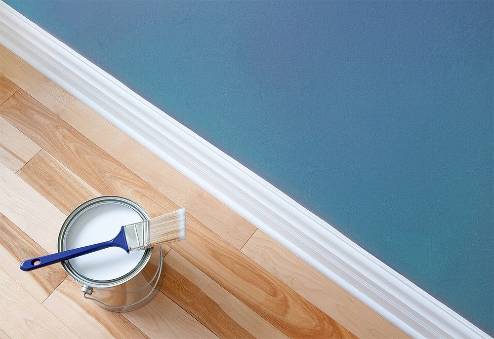 Ein Farbeimer mit weißer Farbe und einem Pinsel auf einem Parkettboden | maler lorenz GmbH & Co. KG